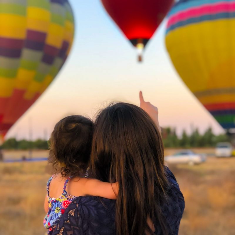 woman carrying toddler point at hot air balloon